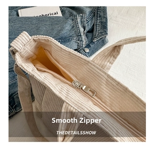 Detailed macro view of the smooth metal zipper and corduroy texture of the beige tote bag
