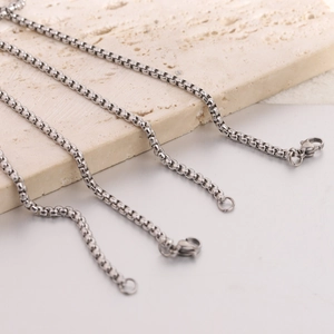 Detail view of silver box chain necklaces with lobster clasp on beige travertine