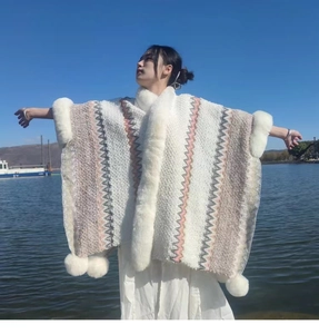Detail of a tribal pattern knit poncho with white faux fur collar and pom-poms by the lake