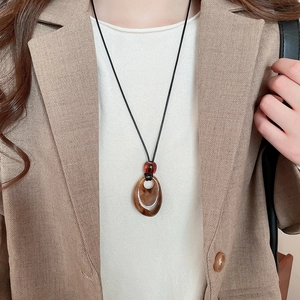 Detail of amber acrylic teardrop pendant on black cord shown on beige blazer