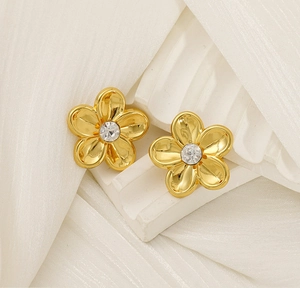 Close-up of golden flower stud earrings with a sparkling center zircon on white texture