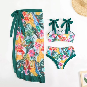 Detailed flat lay of a green floral three-piece bikini set with matching mesh beach skirt