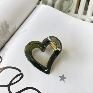 Close-up of heart-shaped dark green resin hair claw clip with golden metal spring