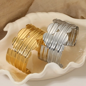 Wide textured open cuff bracelet in gold and silver finish on a white shell plate