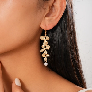 Close-up of golden petal drop earrings with white pearl detail worn by model