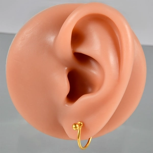 Close-up of a golden G23 titanium nipple ring with a gold ball on a silicone ear model