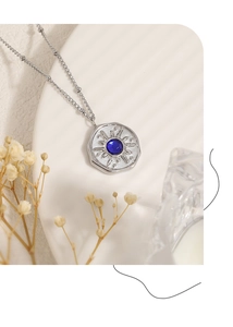 Detail view of the silver sunburst pendant featuring a blue gemstone on a delicate bead chain