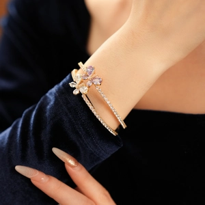 Détail d'un bracelet doré à double rangée avec charms papillon et fleur en zircon violet