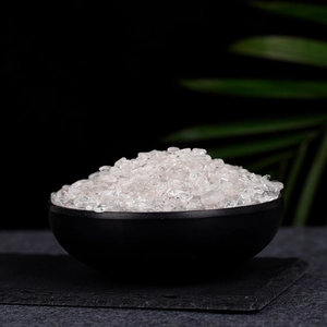 Natural clear quartz crystal chips in a matte black ceramic bowl on a stone base