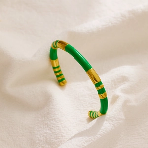 Detail of green enamel and gold bamboo-style stainless steel open bangle on white linen