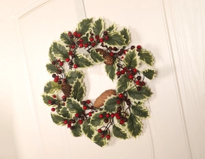 Close-up of Christmas wreath with red berries, pine cones and white edged leaves