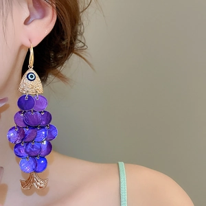 Macro view of gold fish earring with purple sequins and blue evil eye detail