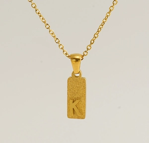 Detail of a rectangular gold-plated letter K pendant with a textured matte finish
