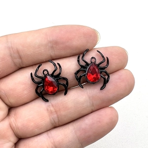 Detail of two vintage metal spider pendants with red rhinestones held between fingers