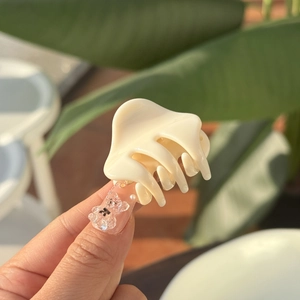 Cream-colored mini butterfly hair claw clip held by hand for scale and styling detail