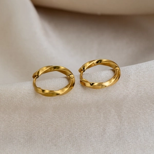 Chic twisted gold-toned stainless steel hoop earrings on minimalist textured fabric