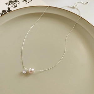 Gros plan d'un collier avec pendentif en perle et zircon sur un plat beige chic