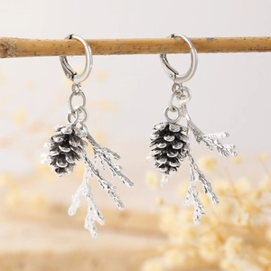 Detailed view of silver pine cone and branch earrings hanging on a rustic wooden twig