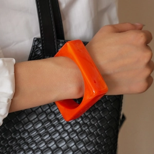 Macro shot of chunky orange square resin bangle styled with a black woven handbag