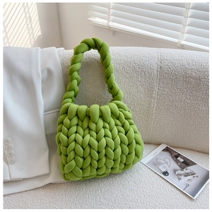 Detail of green chunky yarn handmade bag placed on a soft white sofa with magazine
