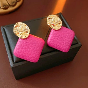Detailed close-up of pink leather earrings with gold irregular textured metal accents
