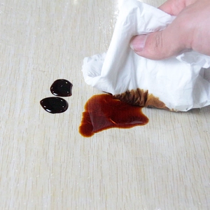 Absorbent white paper towel cleaning brown liquid stains on a textured wooden surface