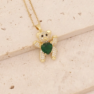 Close-up of golden bear pendant with green heart zircon and crystal stones on stone