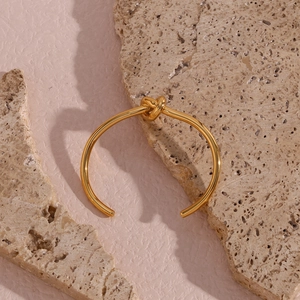Close-up of a minimalist gold-plated knot cuff bracelet on a natural stone background