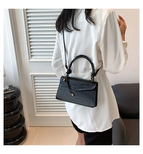Detail of black textured crossbody bag with gold hardware worn by a model