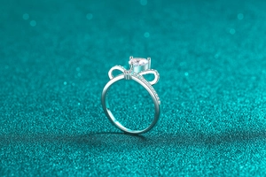 Macro shot of silver bow ring with round center diamond on a sparkling blue background