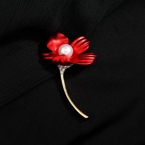 Close-up of red matte flower brooch with central pearl and rhinestone accents on fabric