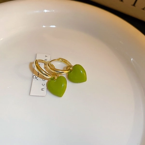 Close-up of gold hoop earrings with green heart pendants on white ceramic plate
