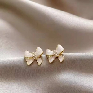 Macro view of gold-plated bow earrings with cream enamel and sparkling crystals