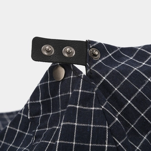 Détail de la sangle réglable en cuir noir et boutons argentés sur la casquette à carreaux