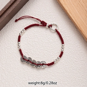 Detailed macro view of Red braided rope bracelet with five silver coin charms on wood