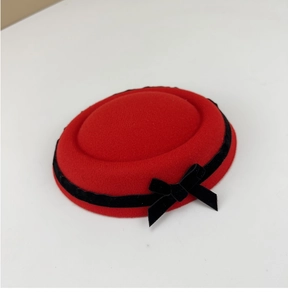Detail of red wool felt pillbox hat with black velvet ribbon and bow on white background