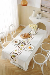 Detail of white tablecloth featuring floral embroidery and decorative tassel edges