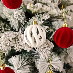 Détail de boules de Noël en velours rouge et spirale blanche sur une branche enneigée