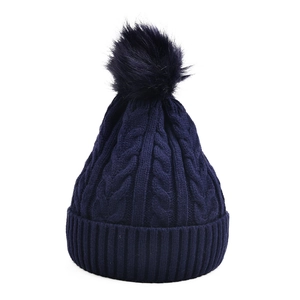 Détail de maille torsadée et grand pompon duveteux sur un bonnet d'hiver bleu marine