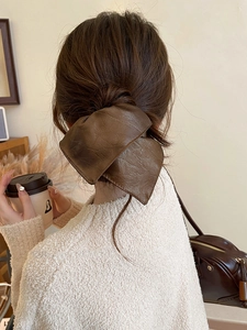 Detail view of large brown faux leather bow hair clip worn by a model in autumn style
