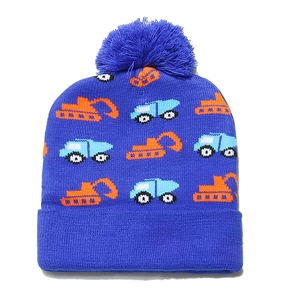Detail of blue knit beanie featuring orange excavator patterns and a fluffy pom-pom