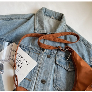 Detail of caramel nylon crescent crossbody bag against a blue denim jacket background