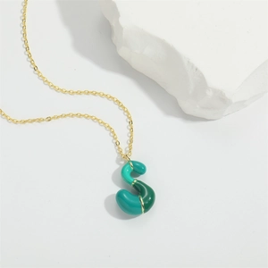 Detail of green enamel S letter pendant with golden accents on a delicate O-chain necklace