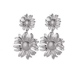Macro shot of silver sunflower petal earrings with layered metallic texture on white background