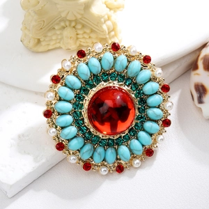 Close-up of vintage gold brooch with red center stone, green crystals and pearls