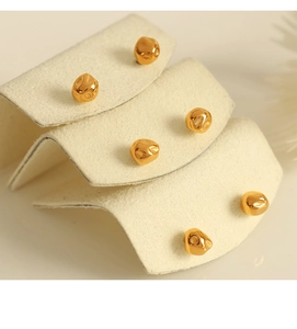 Macro shot of three pairs of golden irregular pebble earrings on a wavy fabric stand