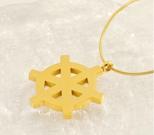 Close-up of golden ship wheel pendant on snake chain over textured ice background