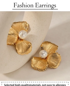 Detail of elegant gold shell-shaped earrings with central pearl on a beige pedestal