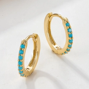 Macro shot of gold huggie hoop earrings featuring inlaid small turquoise blue stones