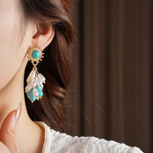 Close-up of bohemian gold earrings with turquoise stones and teardrop pearls on a model